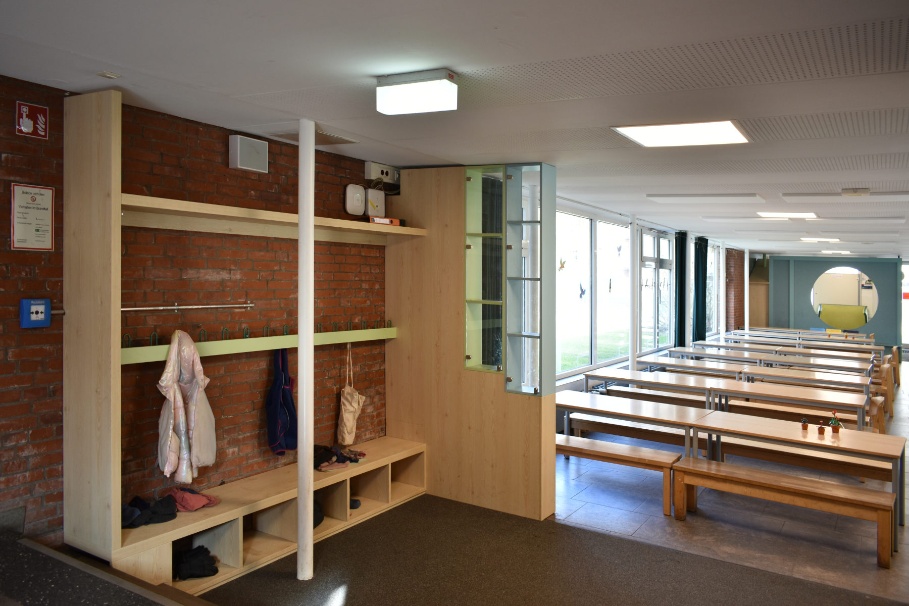 Schulgarderobe mit Sitzbank, Hakenleiste und integrierter Vitrine als Raumteiler zwischen Flur und Aufenthaltsbereich