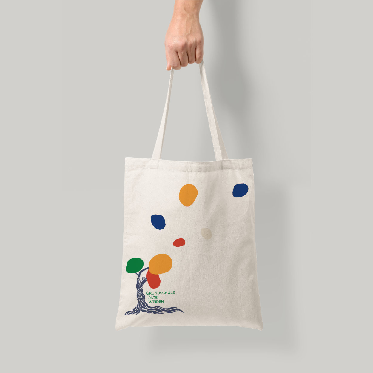 Stoffbeutel mit dem Logo der Grundschule Alte Weiden und farbenfrohen Gestaltungselementen aus dem Designsystem Stoffbeutel mit Logo und bunten Farbkleksen der Grundschule Alte Weiden als Teil des Merchandise-Designs