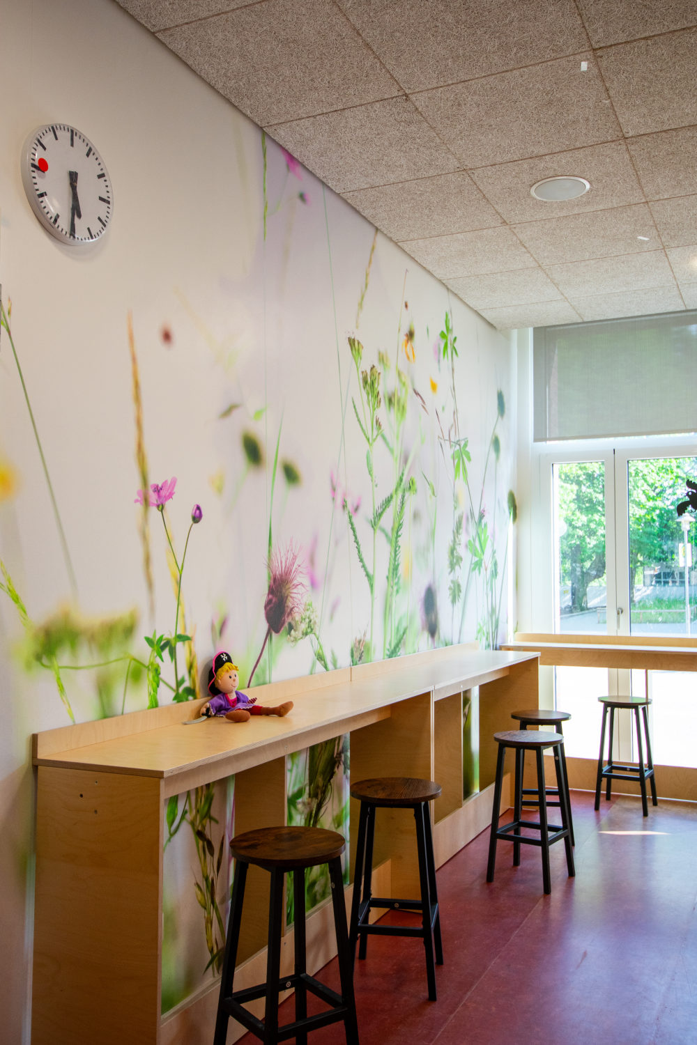 Stehtische aus Holz in der Mensa der Grundschule Nettelnburg, ergänzt durch eine Wand mit Wiesenblumentapete und Ausblick auf den Fensterbereich