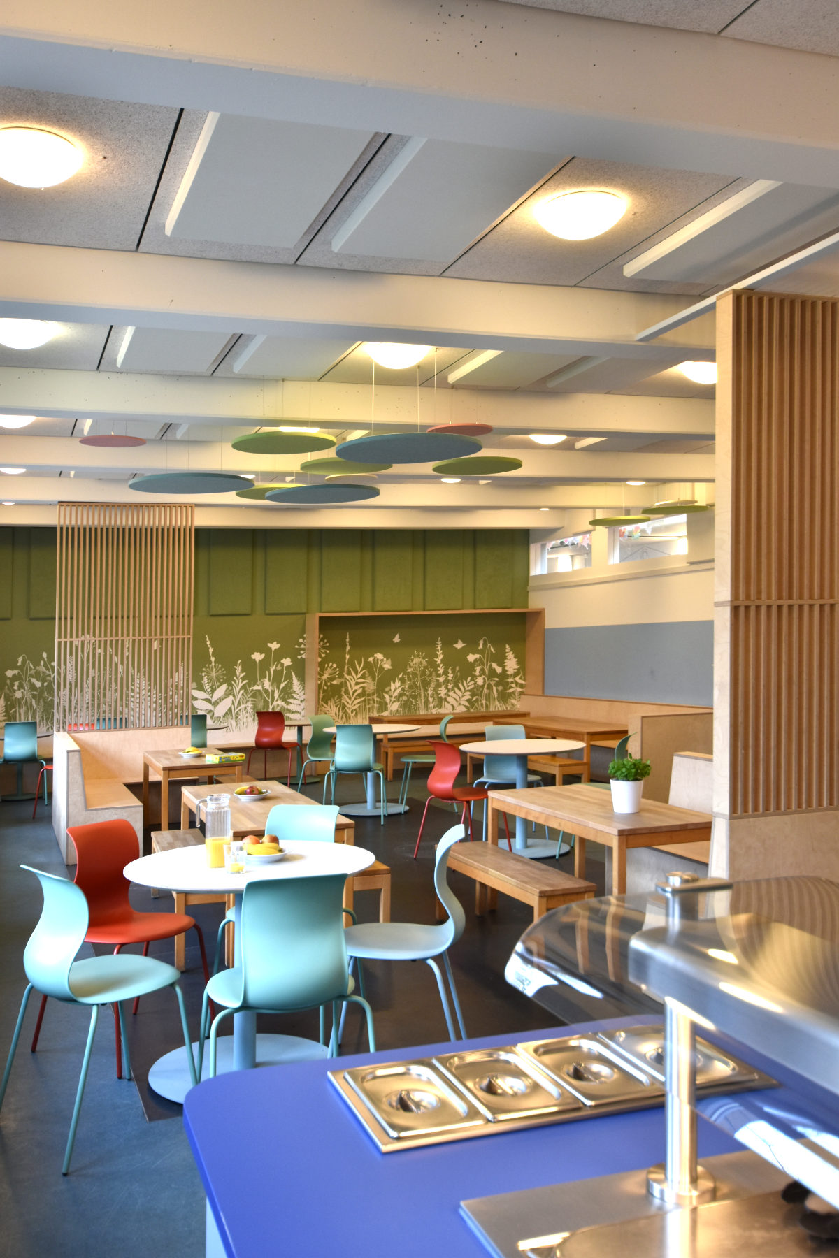 Holzlamellen-Raumteiler in der Mensa der Clara-Grunwald-Schule, die den Bereich der Essensausgabe vom Sitzbereich räumlich abgrenzen.