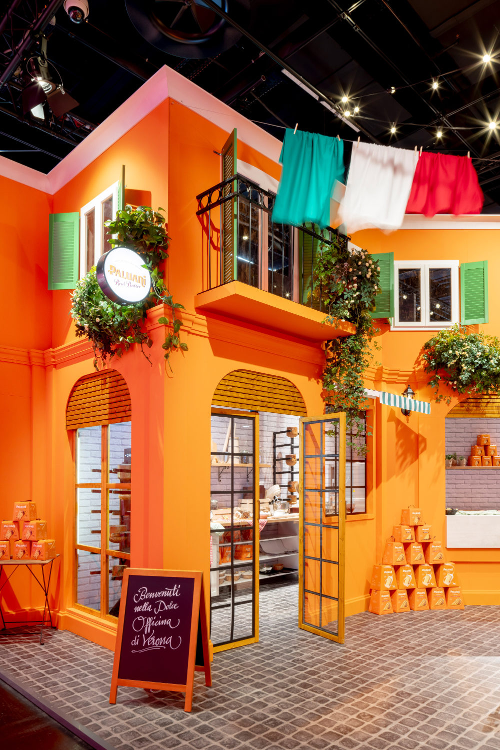 Detailansicht des von Juni Studio entworfenen Paluani Messestands auf der ISM Köln mit italienischer Piazza, Café-Sitzplätzen, Fassadenelementen und Produktpräsentation