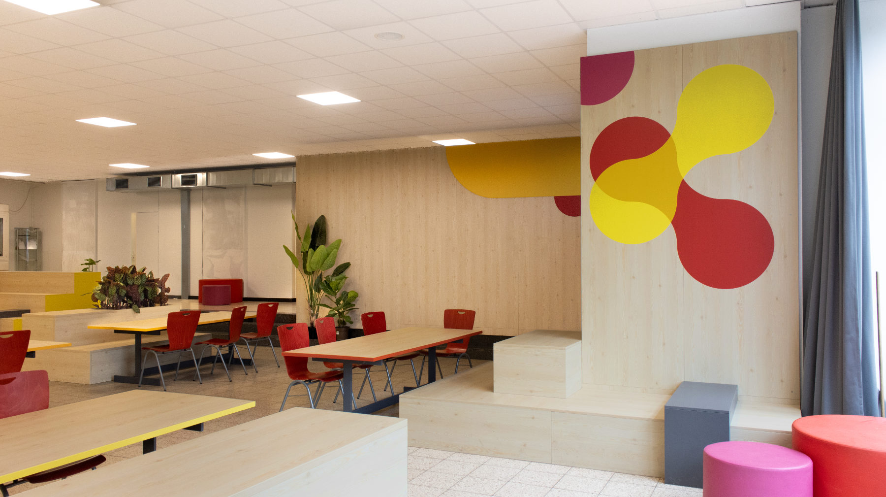 Lange Gruppentische mit roten Stühlen vor grafischer Wandbespielung im Corporate Design der Otto-Hahn-Schule