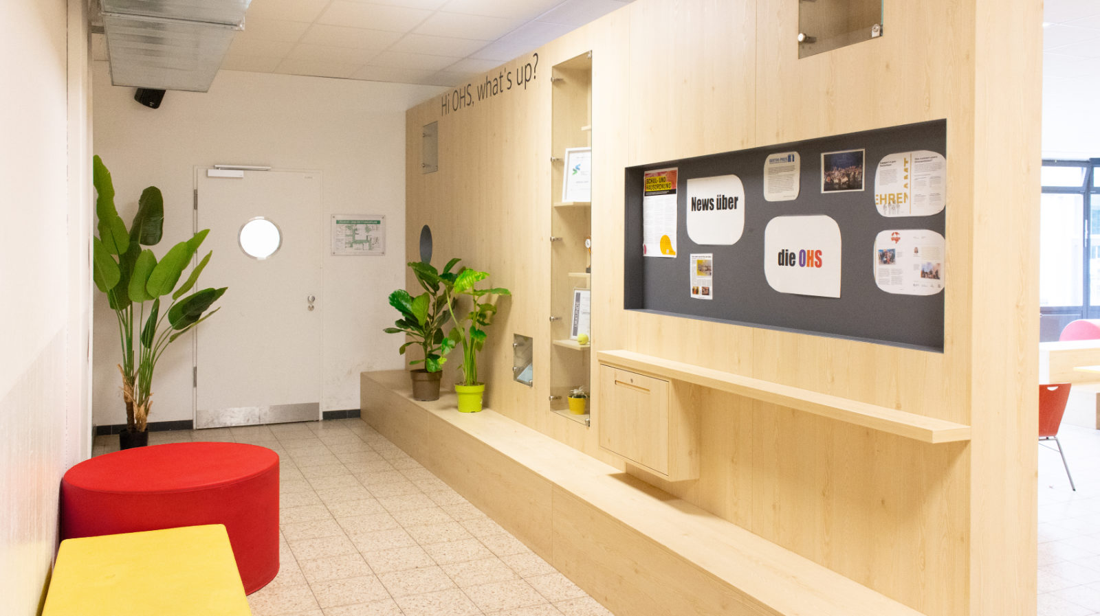 Multifunktionswand mit Pokal-Vitrine, Pinnwand und Sitzbank trennt den Verwaltungsgang von der Pausenhalle der Otto-Hahn-Schule