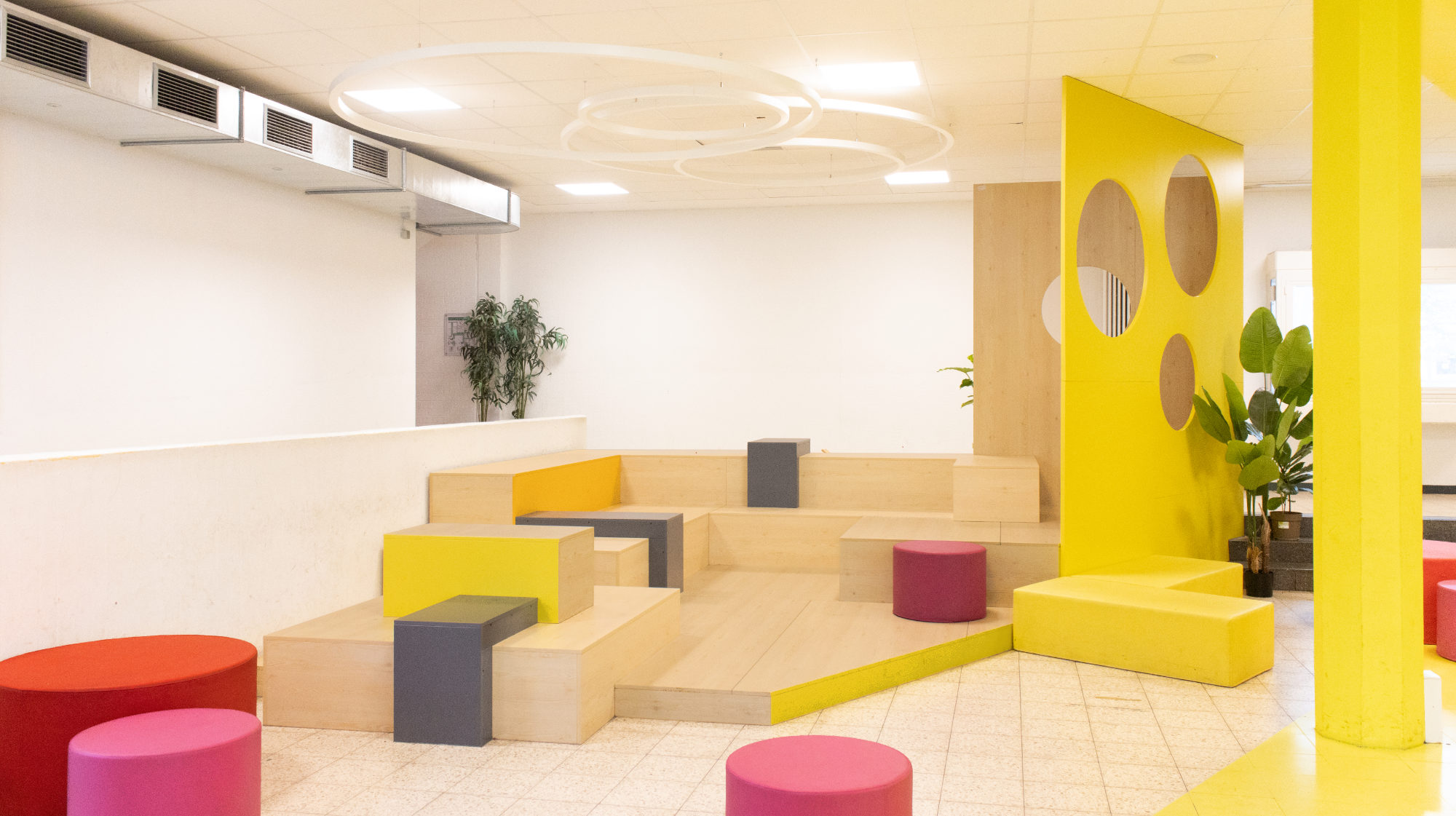 Gestufte Podestlandschaft mit farbigen Sitzwürfeln und runden Ringleuchten in der Pausenhalle der Otto-Hahn-Schule