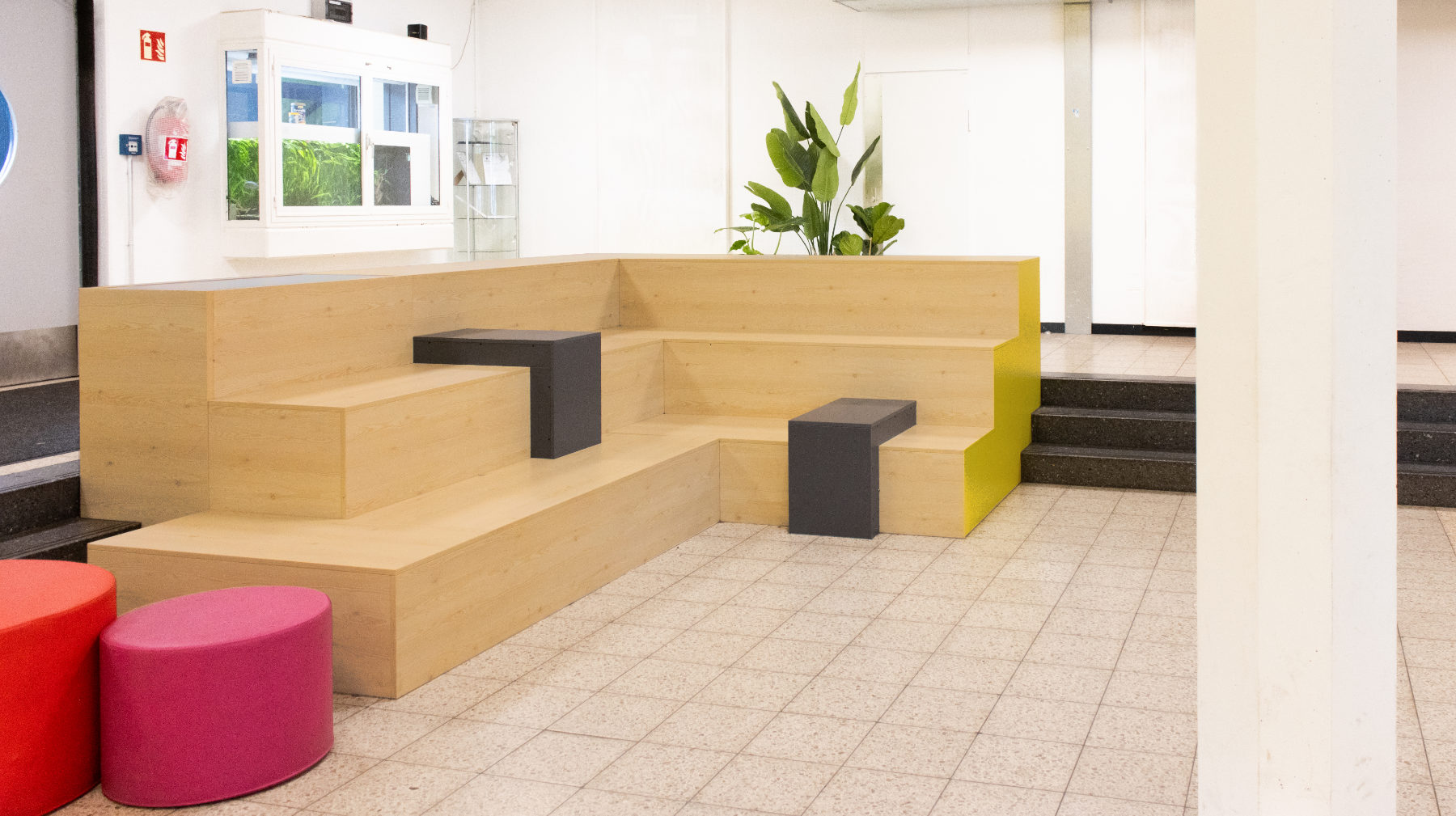 Winkelförmige Sitztreppe mit zwei integrierten, dunklen Tischboxen in der Pausenhalle der Otto-Hahn-Schule