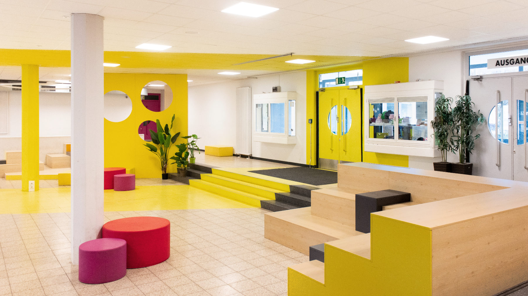 Umlaufende Treppe mit Sitzlandschaften in den Ecken zoniert die Pausenhalle der Otto-Hahn-Schule